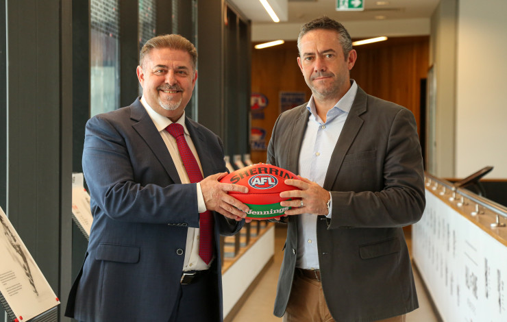 Mayor Cr Jim Memeti shaking hands with St Kilda Football Club Chief Operating Officer Simon Lethlean while holding a football