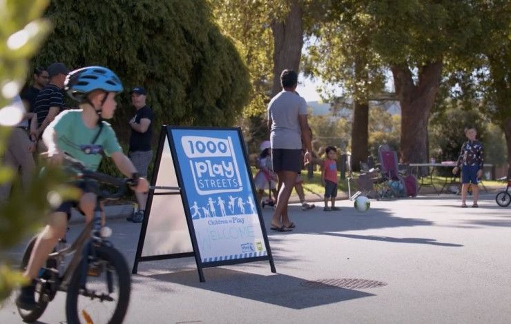 A child riding his bike past a 1000 Play Streets sign