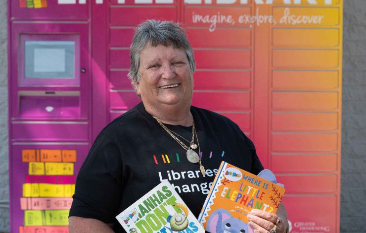 Councillor Angela Long holding children's books in front of the little library lockers