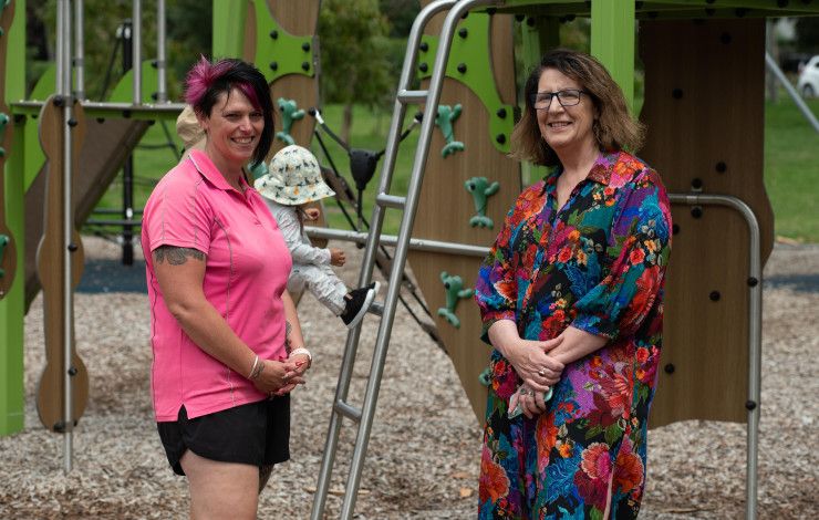 Councillor Rhonda Garad and another lady stand in front of a young child playing at a playground.