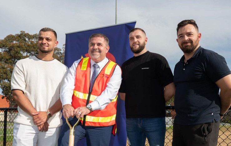 Four men standing together while one leans on a shovel.