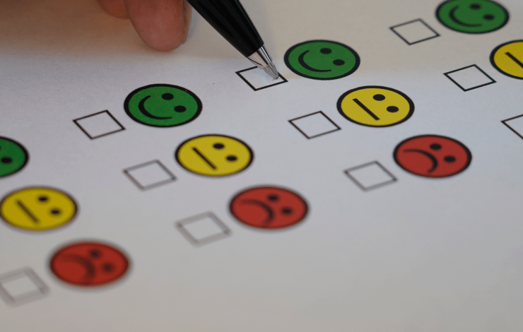 Green, yellow and red smiley icons on paper. A person is ticking the green happy icon.