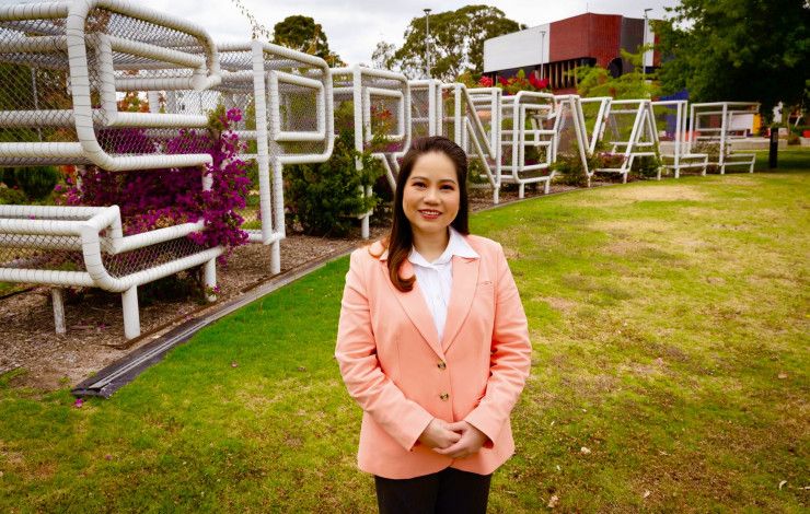 A woman dressed in a light pink blazer standing in front of a metal sculpture spelling out Springvale