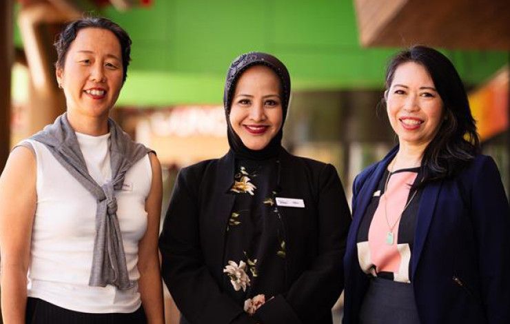 Three women stand in a line and smile at the camera