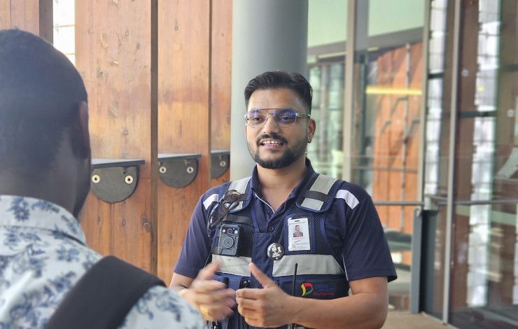 A man dressed in a security uniform talks to another man whose back is to the camera