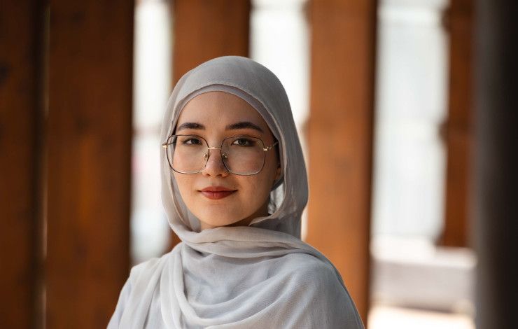 A woman wearing a head scarf and glasses smiles at the camera