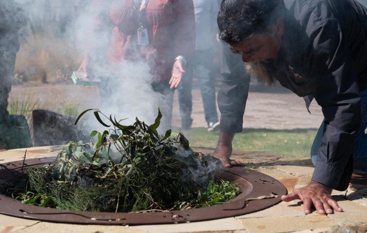An Indigenous Elder creating smoke in a ceremonial fire pit as part of a smoking ceremony