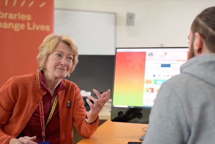 Teacher talking to a young man working at the computer   