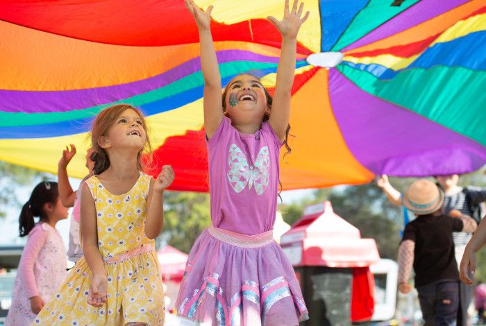 Two children playing under a rainbow parachute