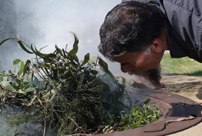 A man blowing on firepit with full of green leaves