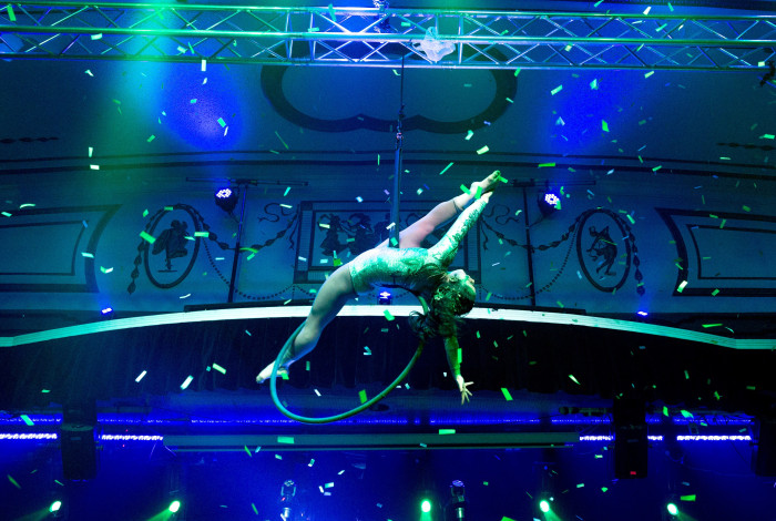 Aerial performer doing acrobatic move inside a hoop, on a stage lit with blue and green