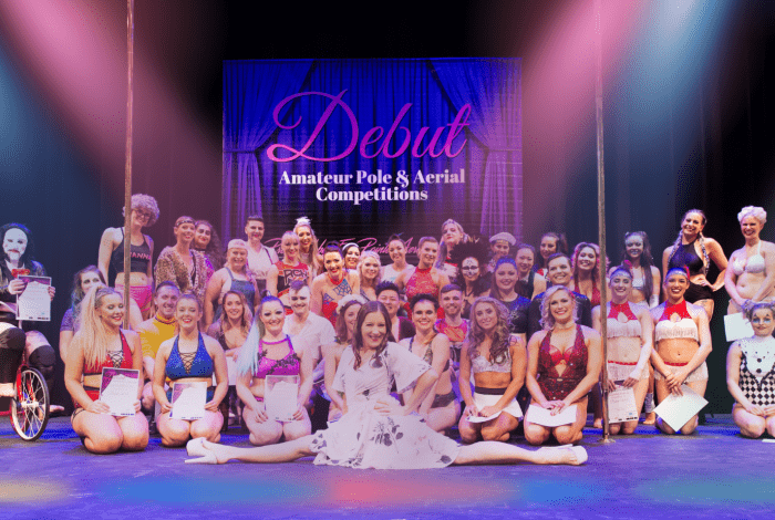 A group of dancers sitting and standing on a stage, smiling and posing with certificates
