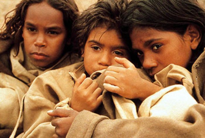 Three young people sheltering under a rug