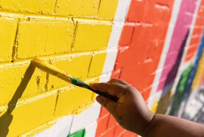people holding paint brushes and painting bright colours on a wall