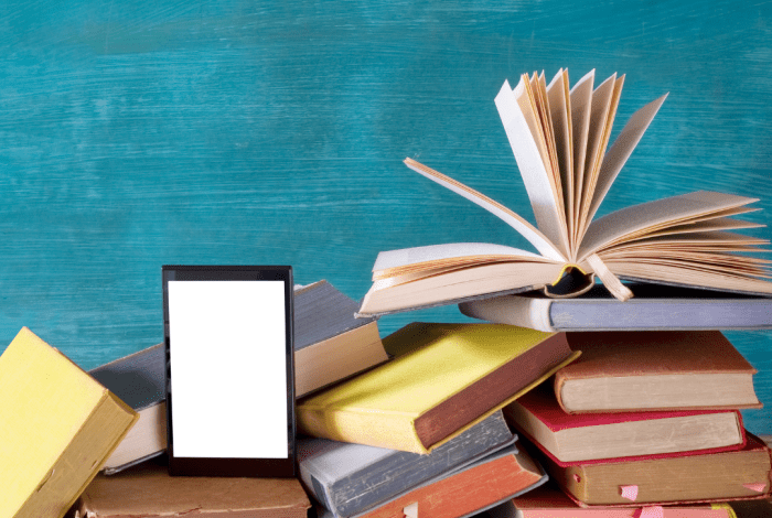 A tablet computer leans facing out from some piles of vintage books