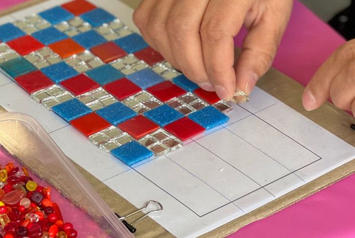 Someone working on a mosaic  template with assorted materials