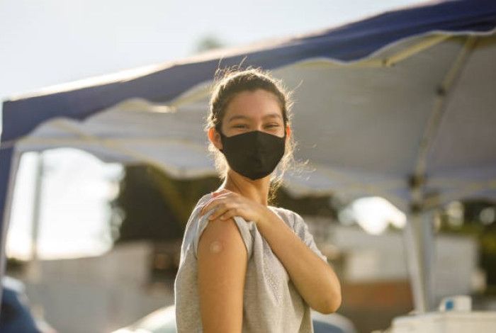 Lady with mask on showing her arm with a bandaid 
