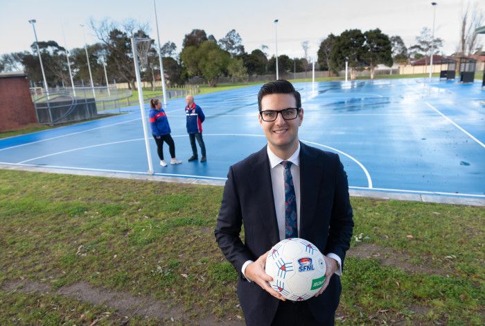 Councillor Tim Dark holding a netball in front of two people talking on a netball court