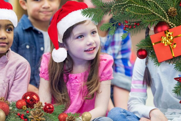 Children wearing chistmas hats enjoying a storytime at the library. A christmas tree and present appear on the right hand side.