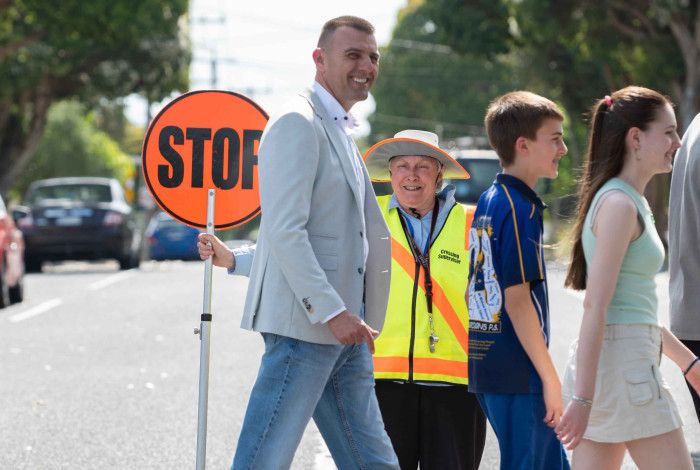People crossing a pedestrian crossing in front of a supervisor with an orange stop sign.