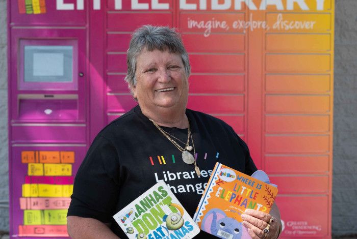 Councillor Angela Long holding children's books in front of the little library lockers