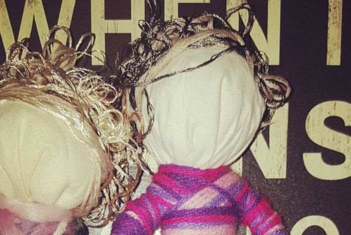 Two handcrafted fabric dolls with yarn hair posed in front of a distressed wooden sign.