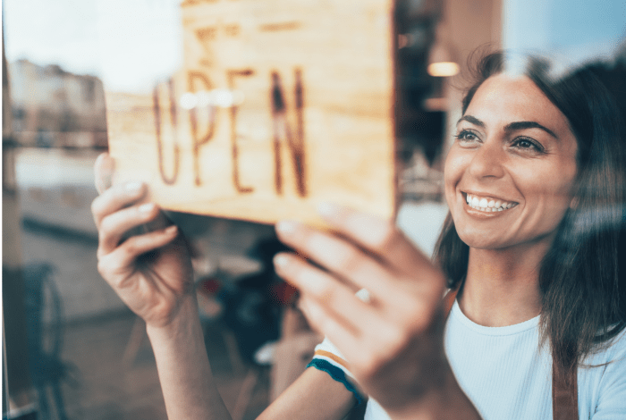 business owner standing at entrance holding open sign