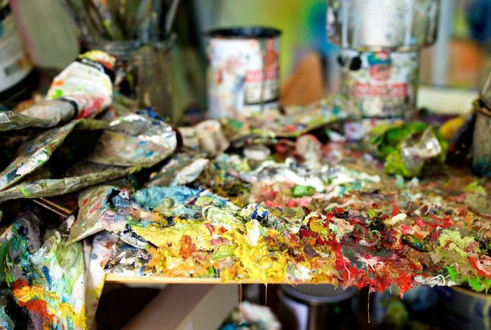 Empty paint tubes and cans covered in dried paint on a table.