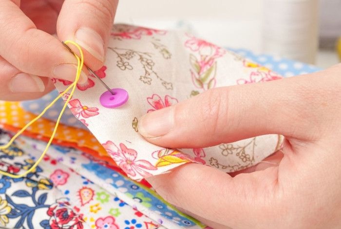 Person sewing button to floral fabric square.
