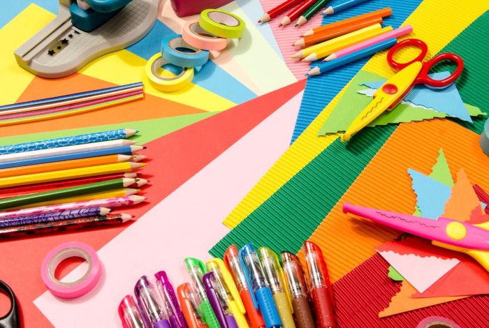 Colourful paper craft supplies including scissors, pencils, washi tape, and textured paper arranged on a table.