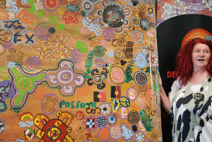 Arist N'Dene Riley standing beside an artwork.