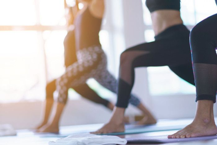 People in a yoga class holding a lunge pose on mats in a sunlit studio.
