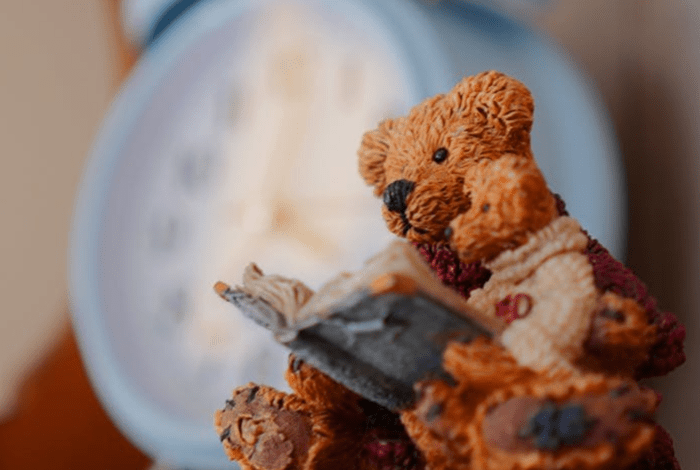 An ornament depicting a teddy bear holding a small teddy and reading a book together.