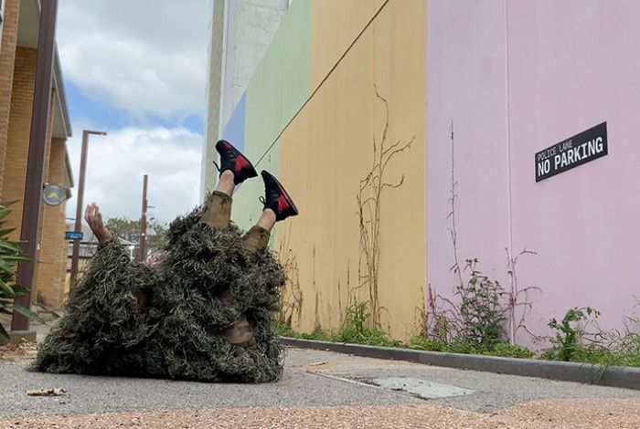 Person in shaggy grass like costume lying on their back in a public lane way