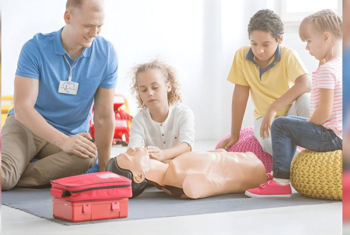 Trainer and group of children practising first aid on a manequin