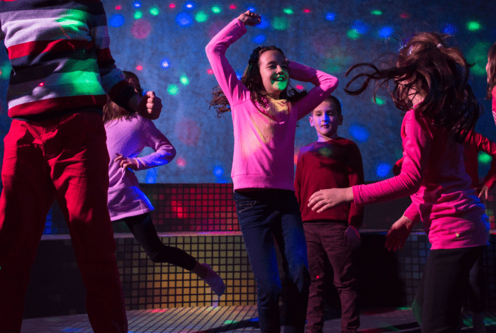 Six children dancing in a dark room with disco lights.