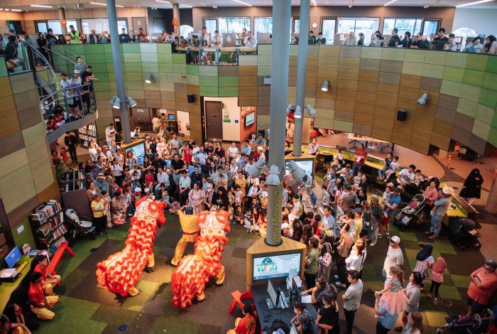 Traditional lion dance at Springvale Library viewed from above, with a crowd of people watching.