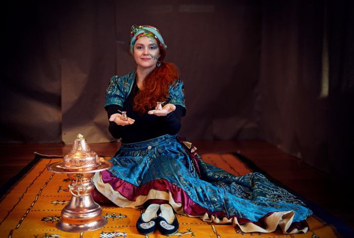 Artist Nela Trifkovic sitting on a rug, wearing traditional Bosnian costume.