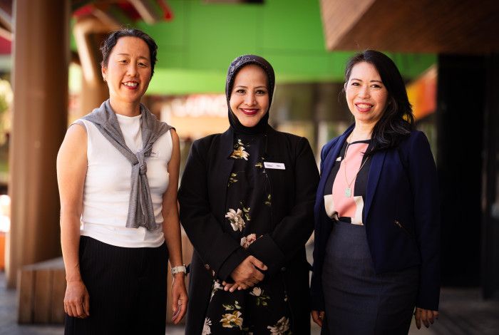 Three women stand in a line and smile at the camera