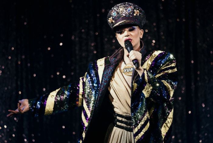 Drag performer on stage with microphone in hand.