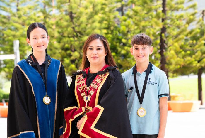 Two smiling children stand either side of a woman dressed in red and black robes