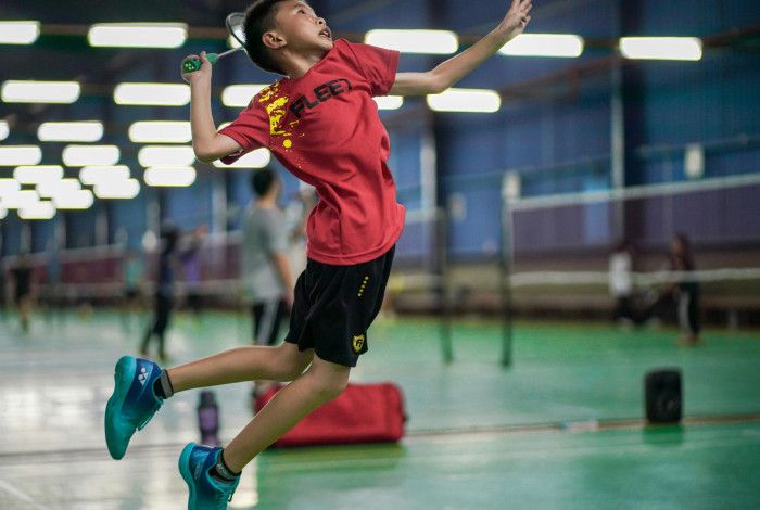 A boy wearing red top playing badminton.
