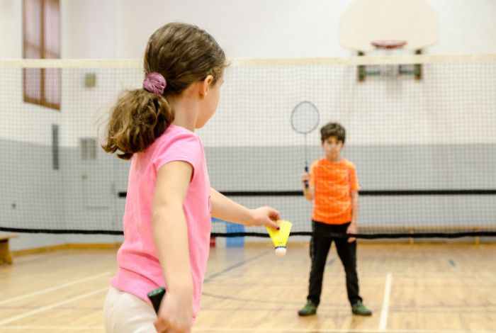 A gidl wearing pink top playing badminton with a boy wearing orange top.
