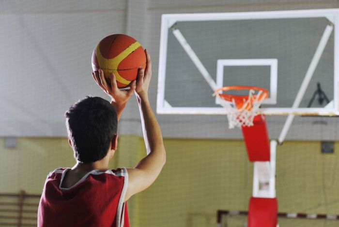 A boy wearing red top is trying to shoot a basketball to the basketball hoop.