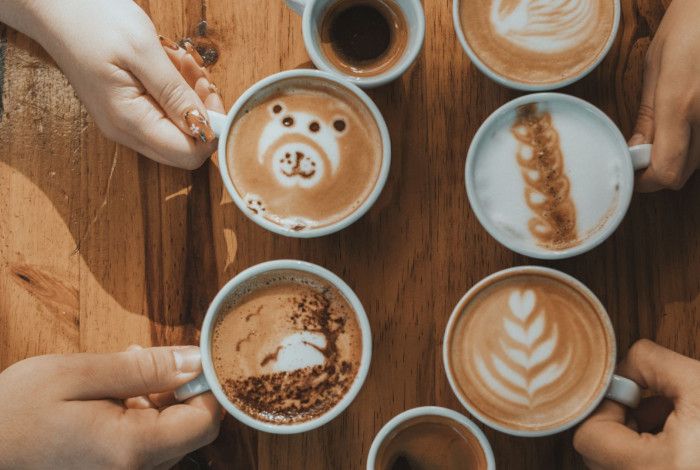 hands holding four coffees on table
