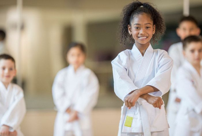 A girl smiling, doing a karate post and wearing white karate uniform, with four boys standing at the background.