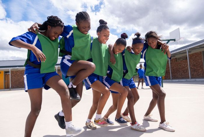 Six girls wearing netball uniform jumping around happily