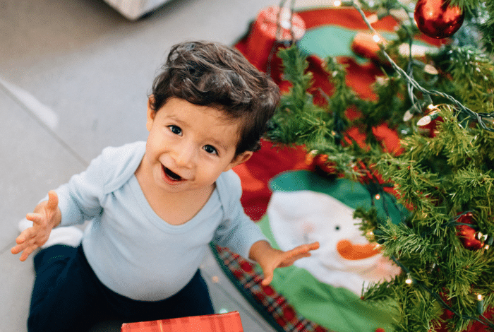 Toddler next to a Christmas Tree, looking up and smiling.