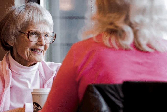 A older woman smiling at another woman over coffee. 