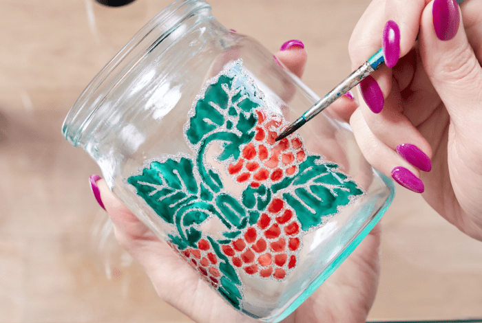 Hands painting raspberries on a glass jar. 